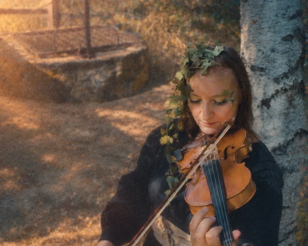 Hilbi joue du violon, adossée à un bouleau, une couronne de lierre dans les cheveux